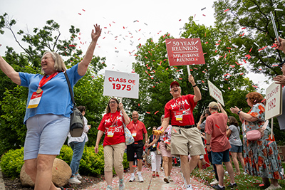 alumni walking in the parade of classes. one alum holds a class of 1975 sign, another holds a 50 year reunion sign