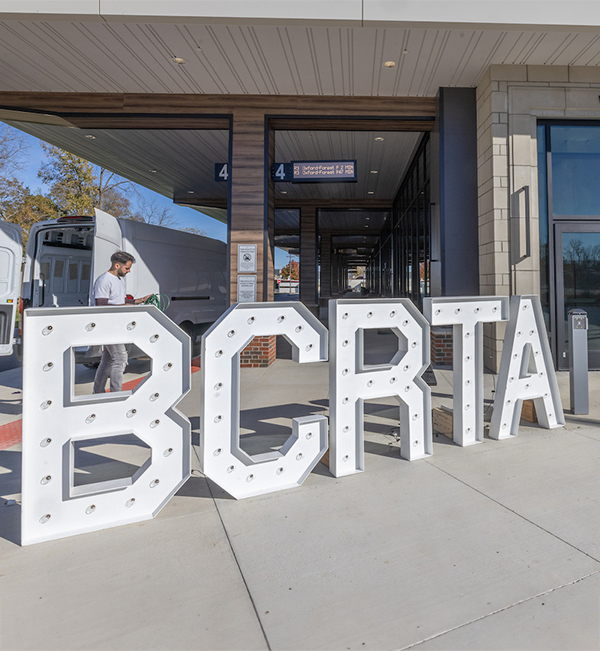 Miami parents pose for a photo op with their student in front of a huge lit up sign that says Family Weekend