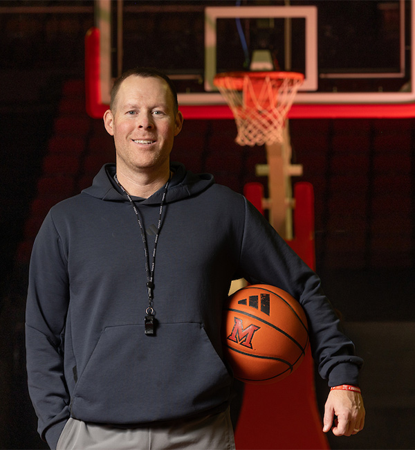 Coach Travis Steele holding a basketball in front of a hoop