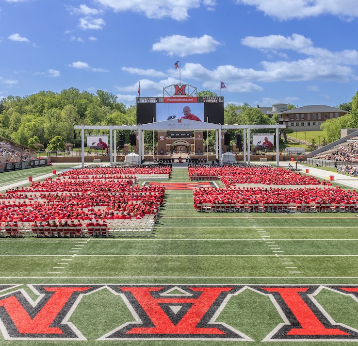 Miami University students arranged in rows across Yager Stadium at spring commencement in front of a stage