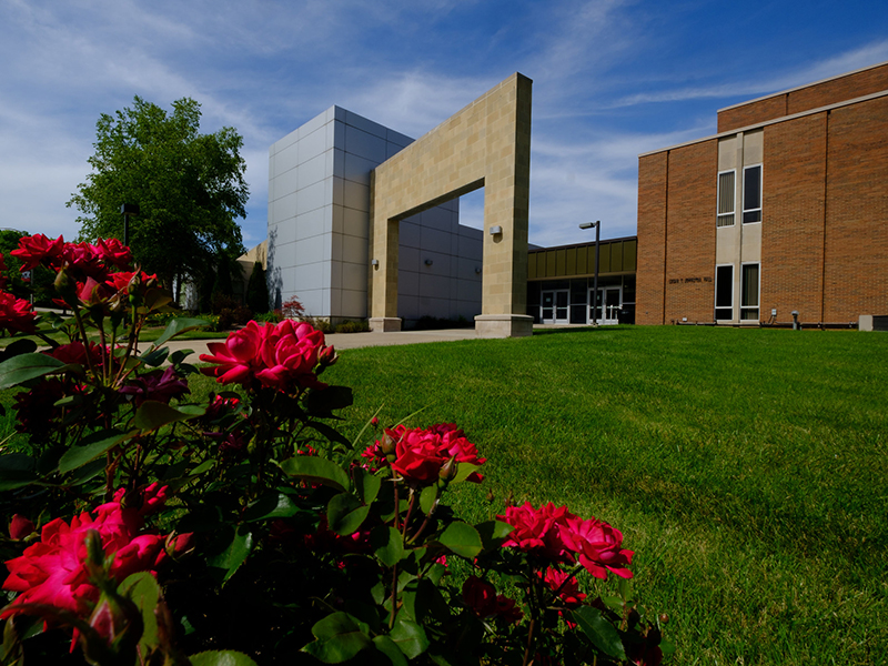 Exterior of Johnston Hall on the Middletown campus with red roses growing on a bush in the foreground.
