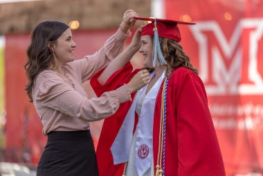 Woman adjusts the graduation cap for a graduate.