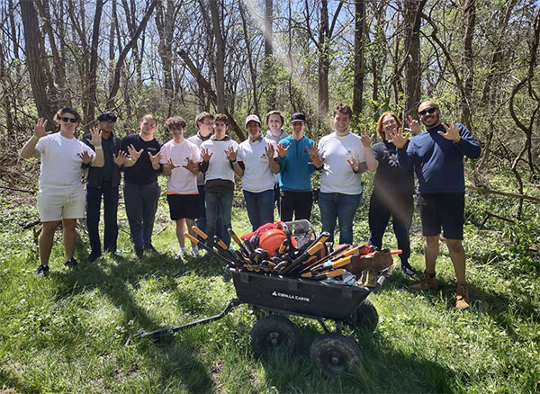 a group of students pose with a wheelbarrow of tools for removing honeysuckle from the natural areas