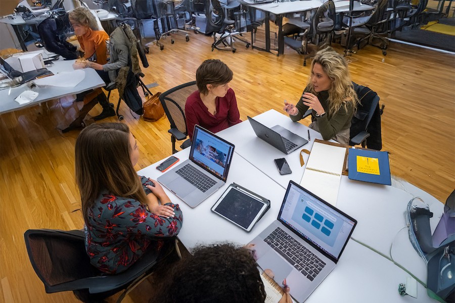 Instructor working with 2 students at a table with their laptops