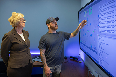 Two individuals collaborate at computer workstations, analyzing data on multiple screens in a tech-focused environment.