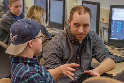 Students engaging in a discussion while collaborating on a computer project in a classroom setting.