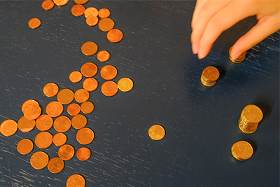 A collection of coins spread out on a surface, with a hand sorting and stacking some of the coins.