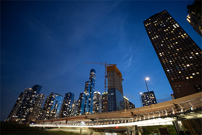 A twilight cityscape featuring skyscrapers and a construction site, illuminated by city lights.