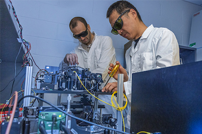 Researchers working with laboratory equipment while wearing protective sunglasses.