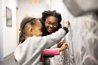 A woman and a child are joyfully drawing on a chalkboard wall, showcasing a creative and interactive learning environment.