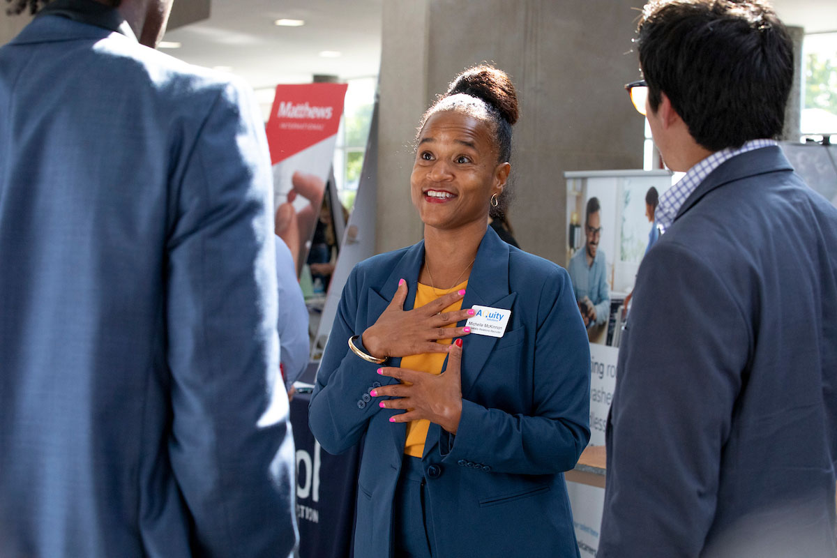 A woman in a business suit smiling and talking with students at a career fair