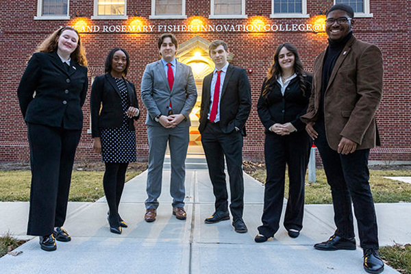 Government relations network students stand in front of the College at Elm building wearing business attire.