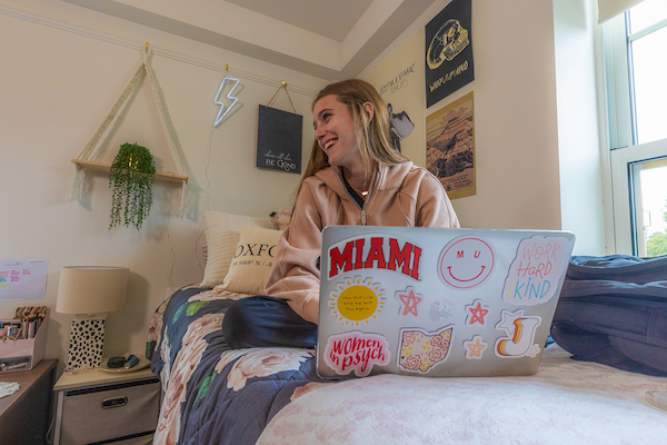 Student sitting on her residence hall bed with her laptop.