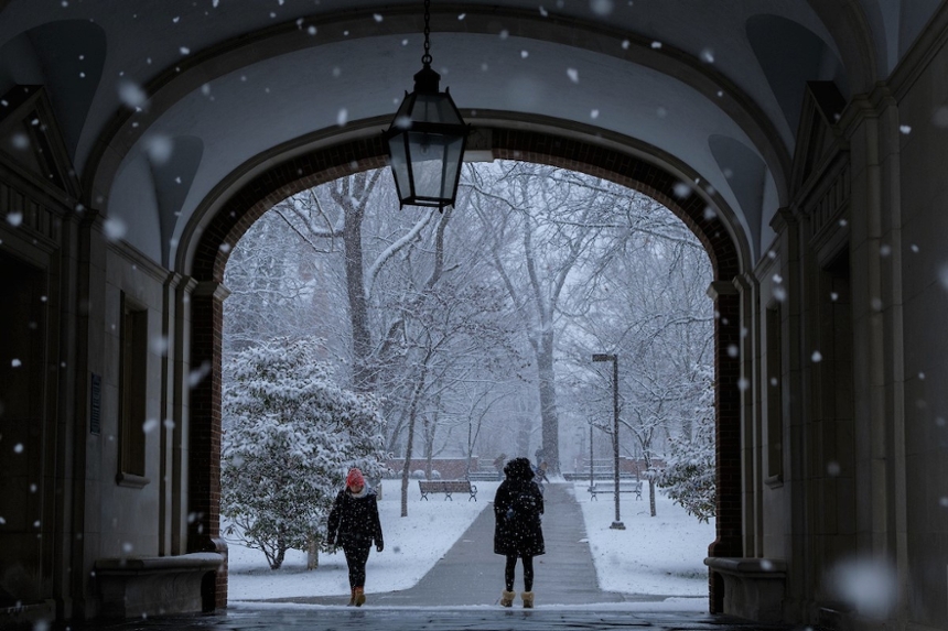 Two students walk near the Upham Arch while snow falls around them.