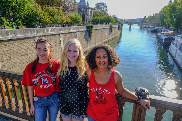 Tres estudiantes en un viaje de estudios en el extranjero parados en un puente sobre un río.