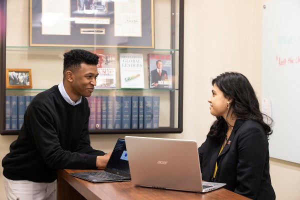 Estudiante sentado con un asesor frente a una computadora