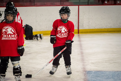 two children in hockey uniforms skating in an ice rink passing the puck to each other