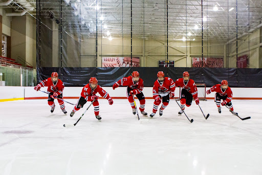 six youth hockey players in uniform skate racing each other with hockey sticks