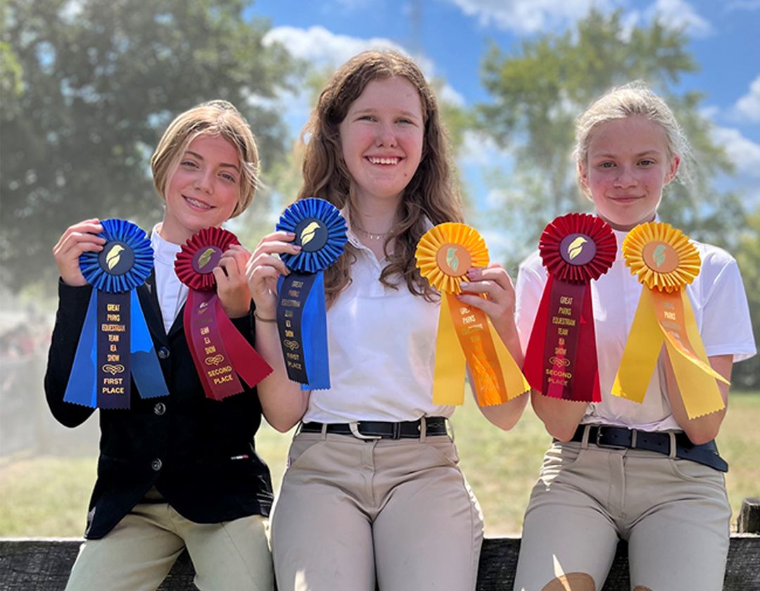 One of the equestrian youth teams sitting on a fence holding up the ribbons they won at a horse show