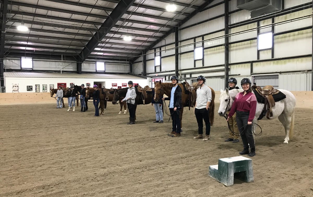 Miami students posing with their horse by their side in the arena