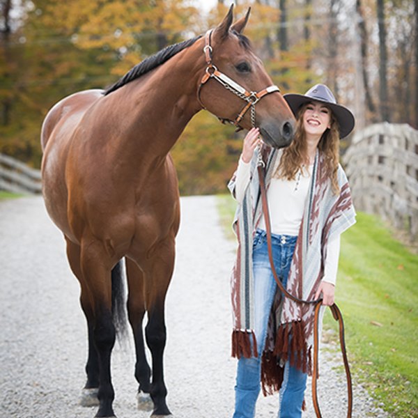 Shelby Zimmerman standing next to her horse while the horse nuzzles her face