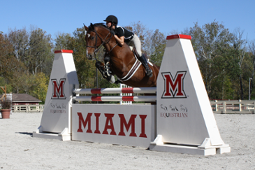Miami student riding a horse while jumping over a large hurdle