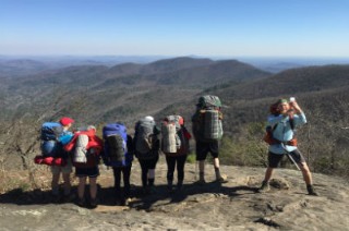 Group on top of a mountain that they just hiked overlooking distant mountains