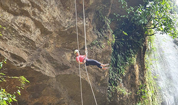 Student rappeling down a cliff wearing a harness and helmet