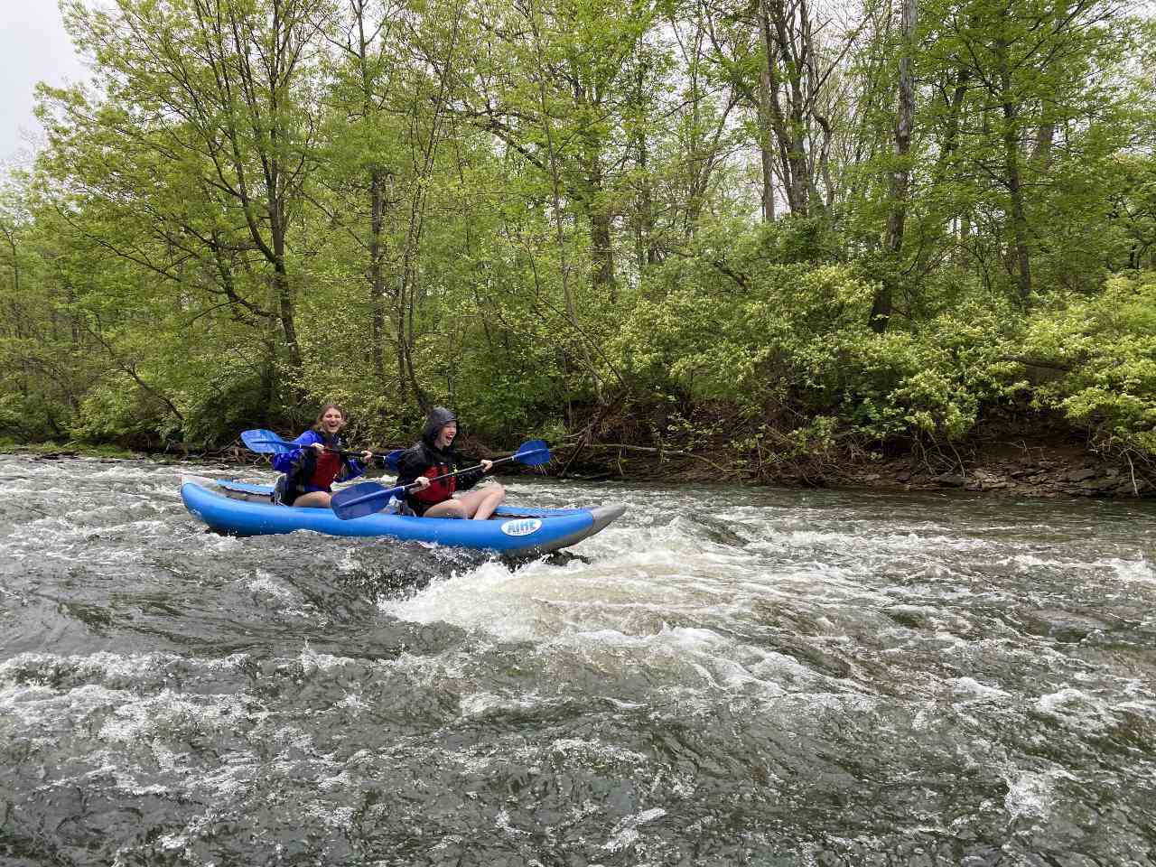 Two Miami students enjoying a kayaking trip in front of vibrant green scenery