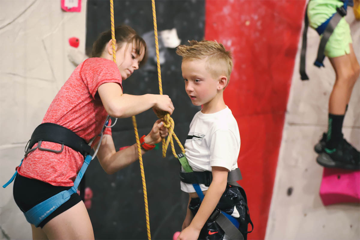 Child climbing the wall wearing a harness with ropes