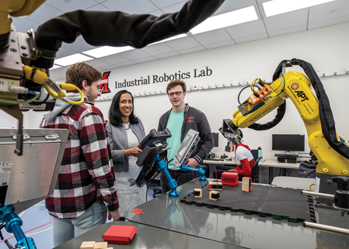 two students and a professor working with robots in the robotics lab