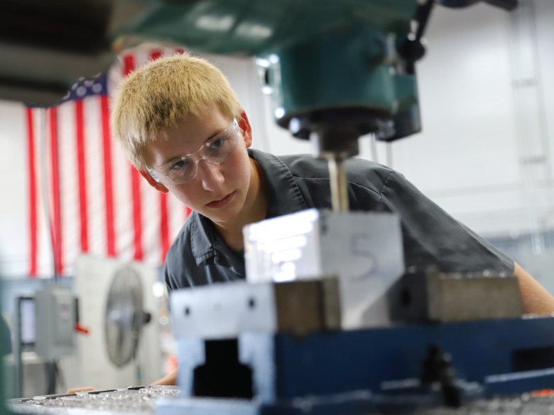 A student wearing safety googles while using a manufacturing machine. 
