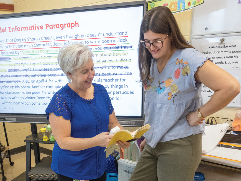 A student teacher standing in front of the class in front of a whiteboard talking.