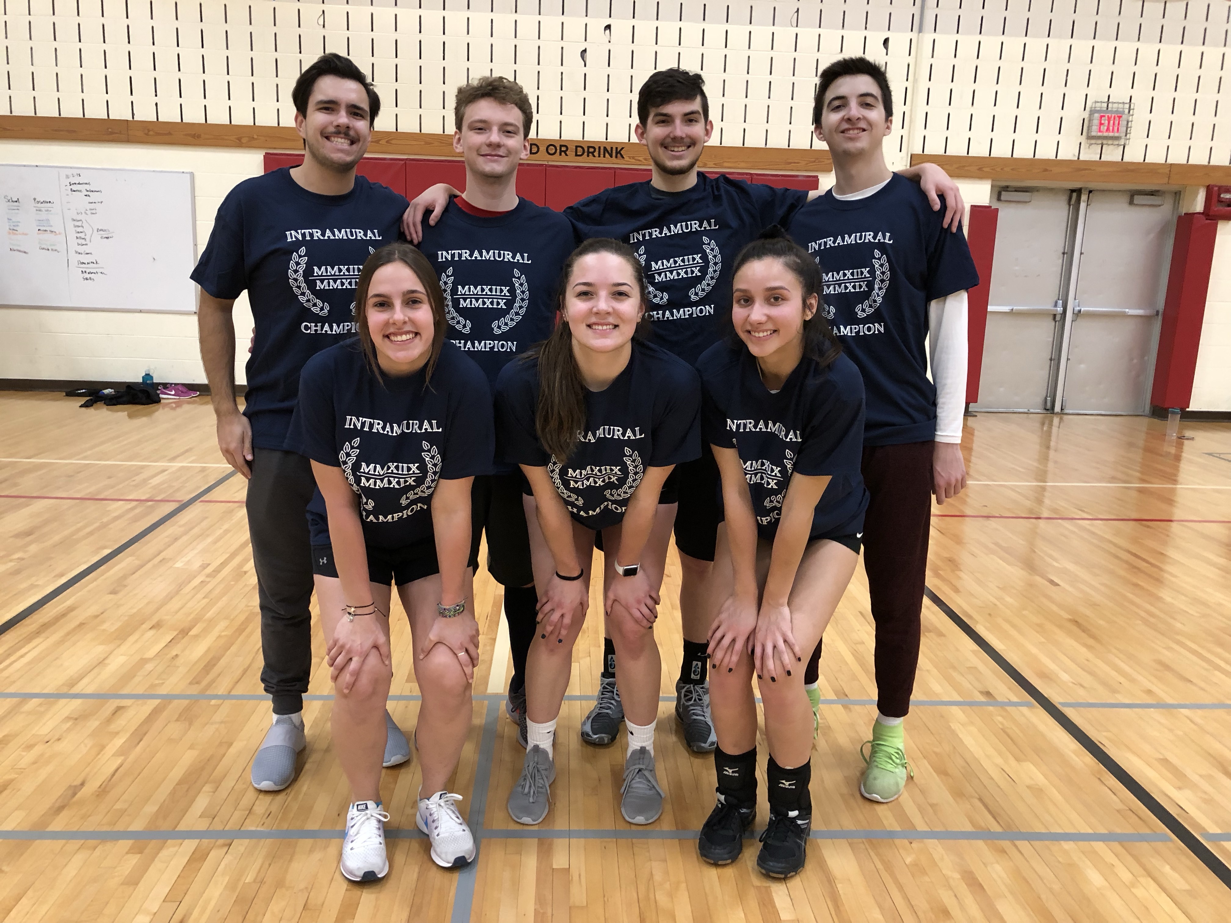 Indoor Co-Rec Volleyball champions team poses in front of the volleyball net in their Intramural Champions shirts.