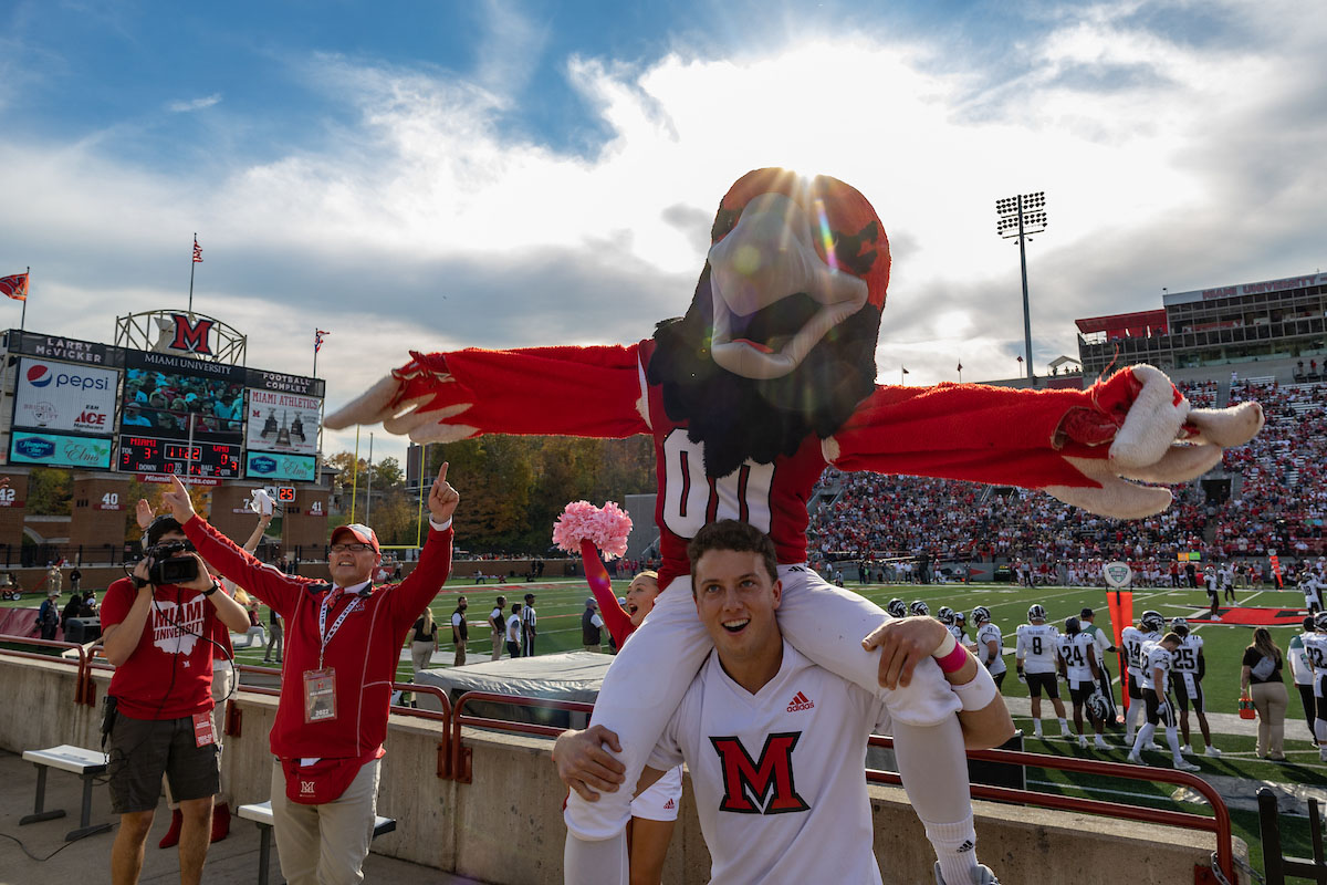 Miami's mascot rides the shoulders of a football player in front of the stadium crowd