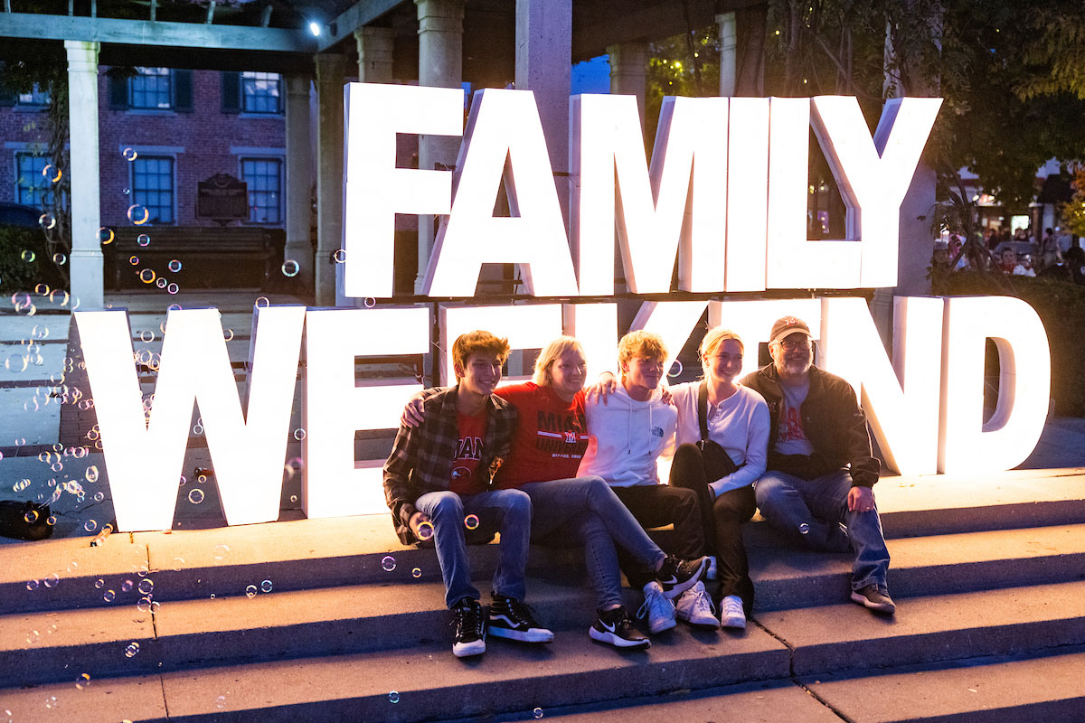 Miami students and their family gathered for a group photo in front of a lighted sign reading "Family Weekend"