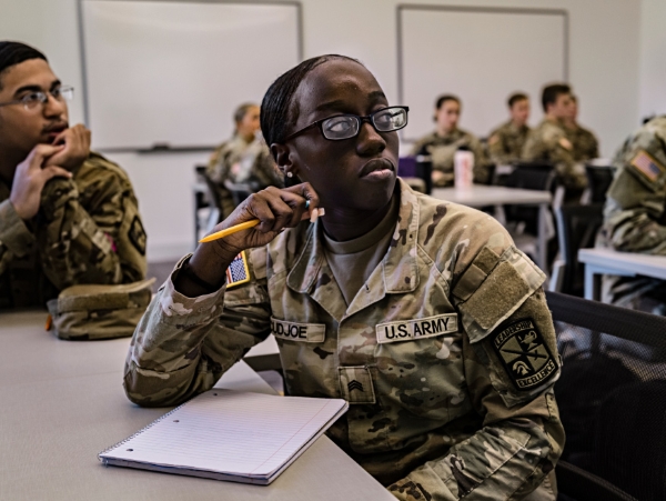 U.S. Army service member in uniform taking notes with a pencil during a classroom training session.