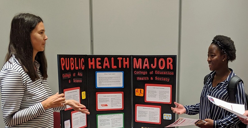 Students talk to program director (left) in front of a table at the health fair.