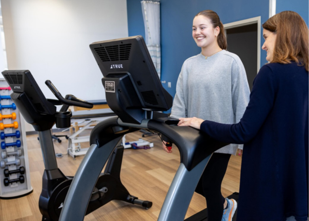 Student on treadmill while faculty stands on the side and speaks to them