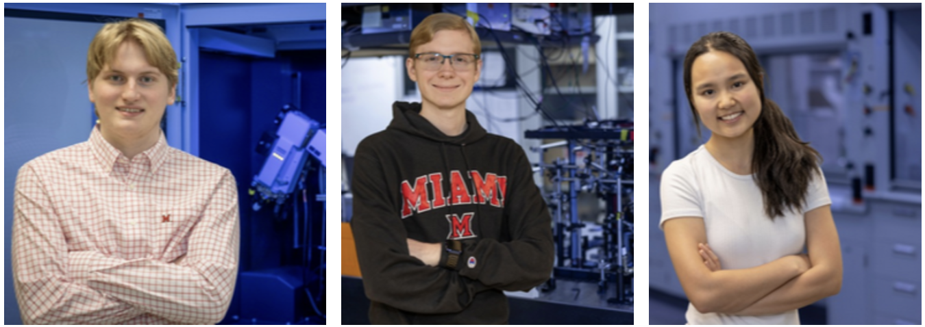 Three young individuals smiling confidently, standing against a backdrop of scientific equipment, representing a collaborative or academic environment.