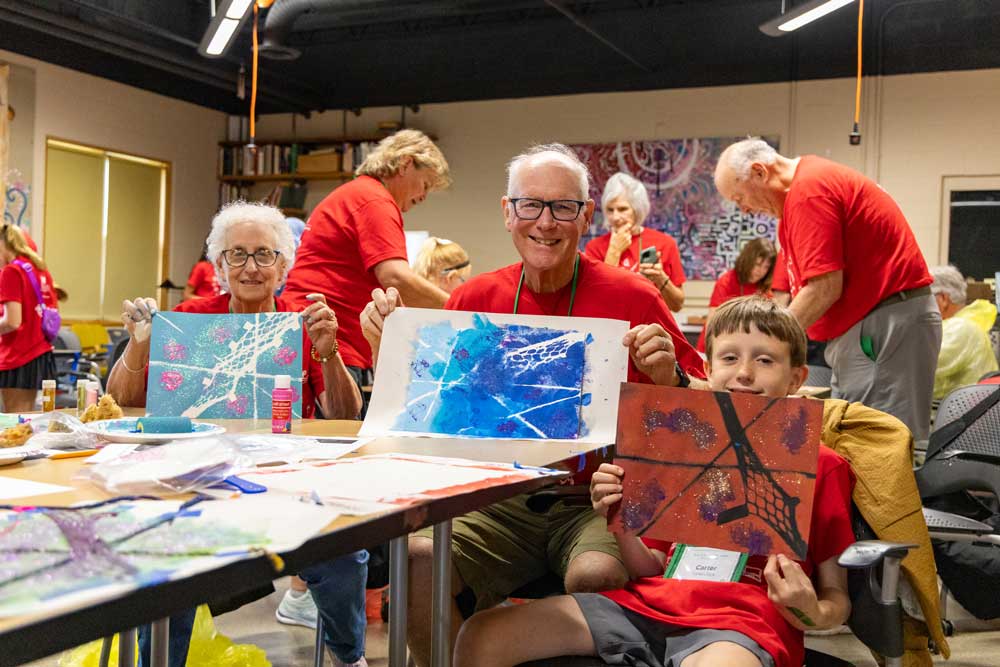 A grandfather and grandmother with their grandson holding up OMA artwork to the camera. 