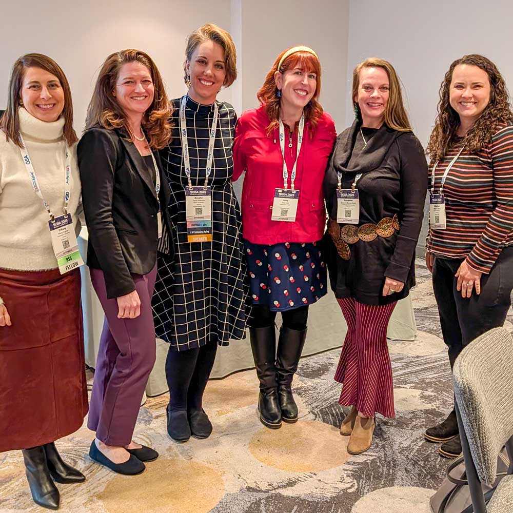 A group of 6 women posing for picture with GSA badges hanging from their necks. 