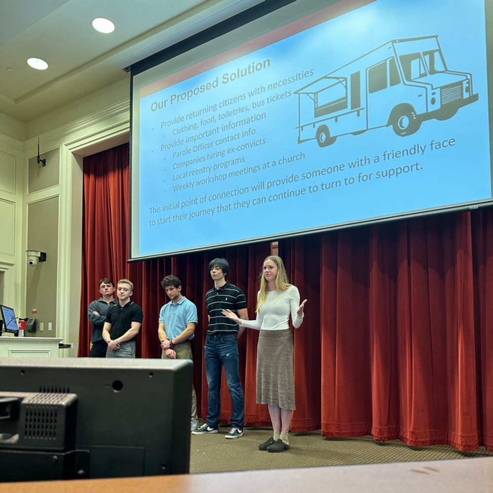 Group of 5 students on a stage presenting in front of an audience.