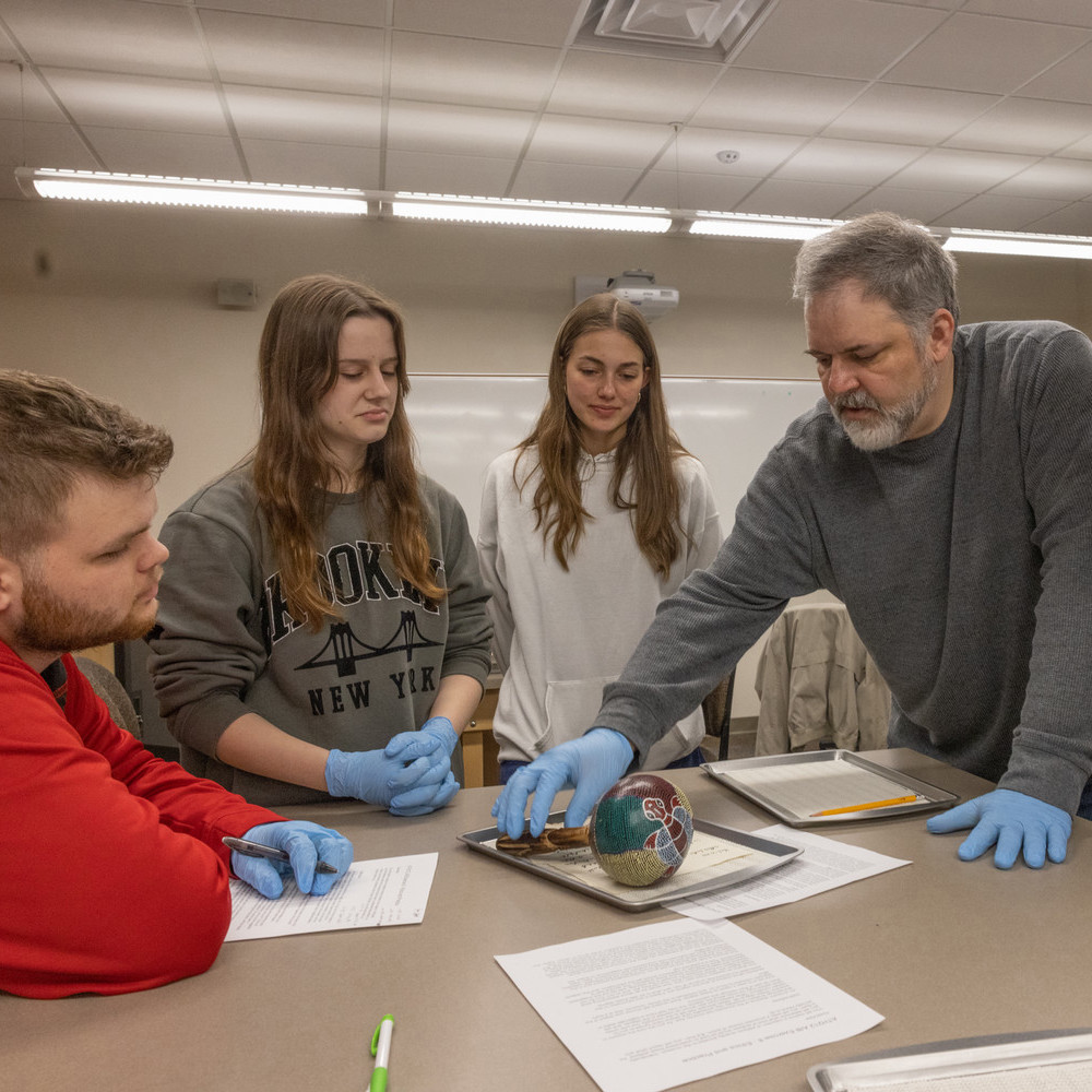 Dr. Jeb Card and students, all wearing blue gloves, handle a spherical artifact.