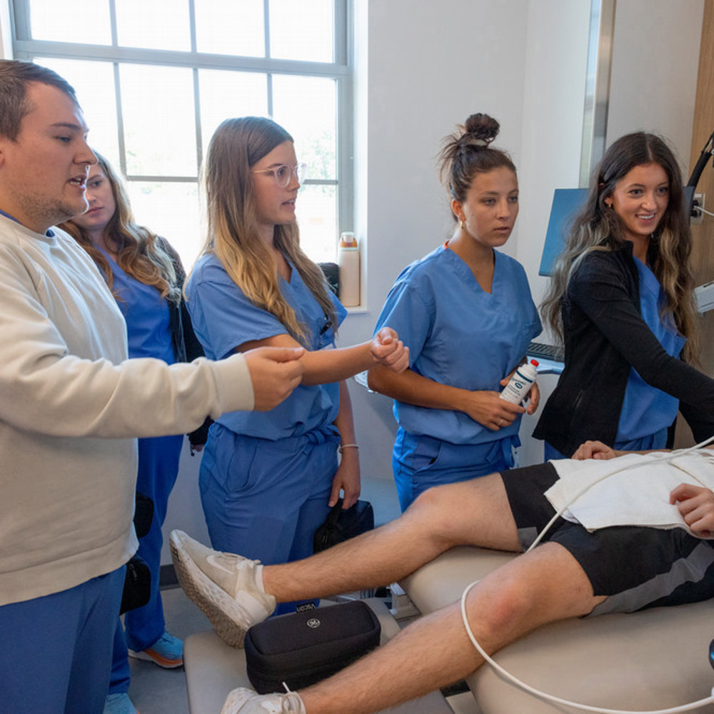 A group of nursing students work with a patient who is laying on a hospital bed.