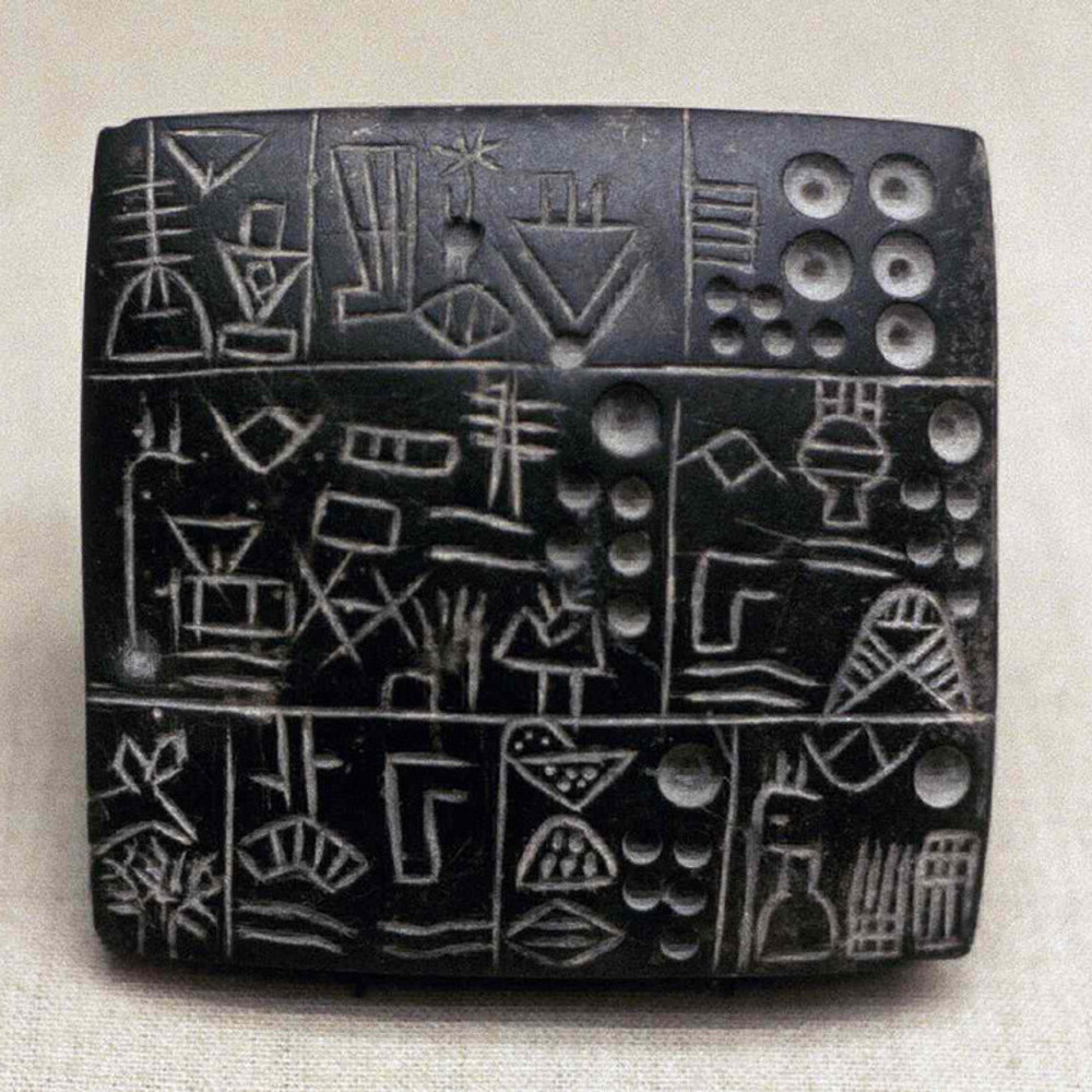 A black stone tablet with cuneiform writing on it with sharp angles and divets.