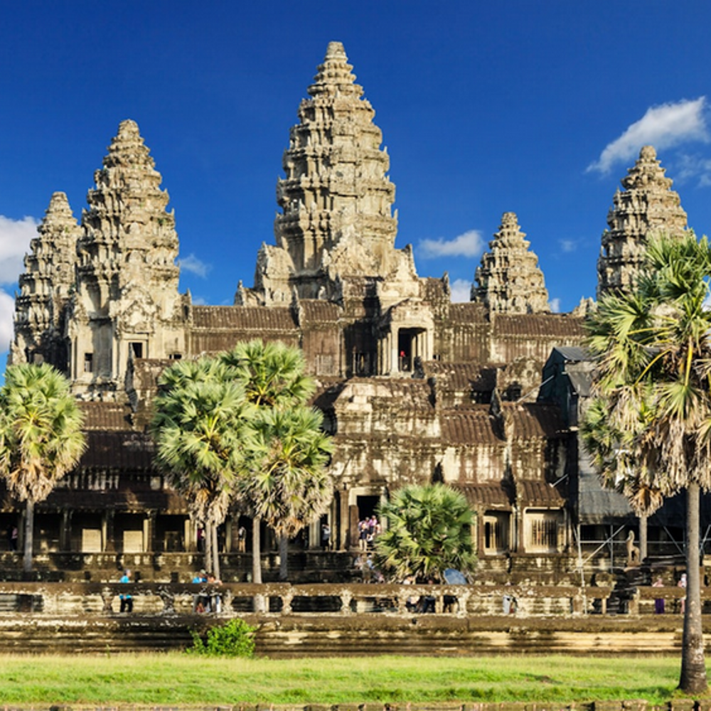 A picture of Angkor Wat, a Buddhist temple which is the largest religious structure in the world. It's made of rugged stone and has three towers that are tiered.