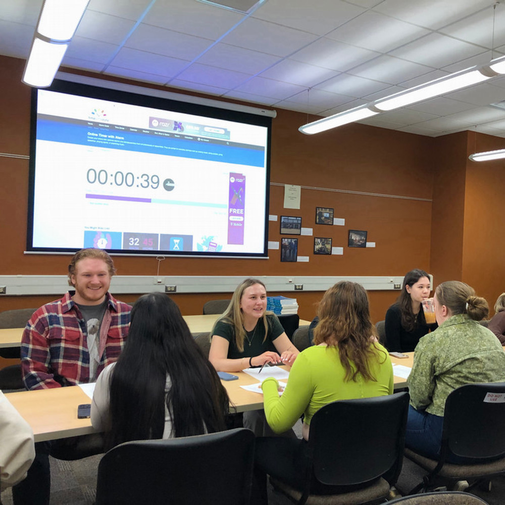 A group of students talk at a table with a timer on the projector in the background.