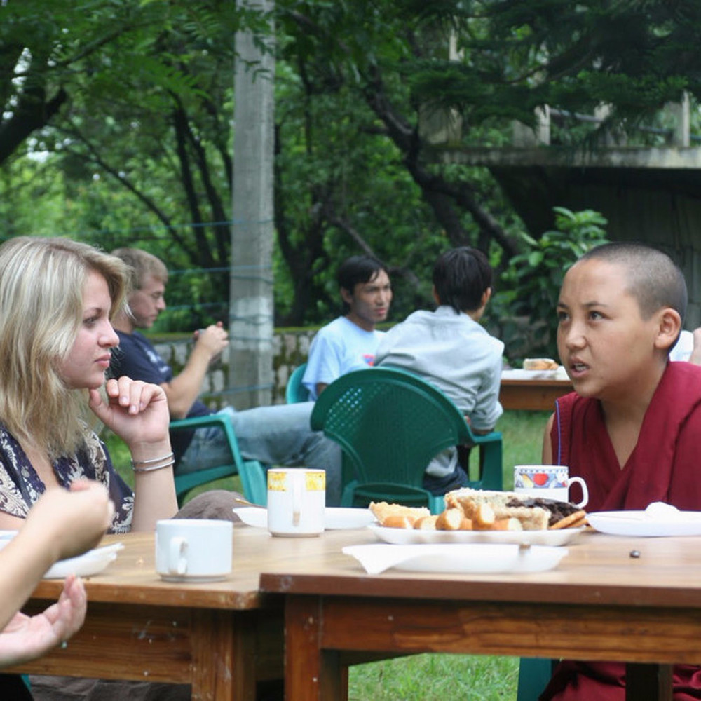 A young Buddhist monk sits at a table with two women, having a conversation.