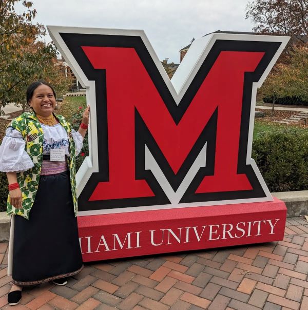 Margarita Fuerez, Vice President of the Panecillo Community standing next to the red Miami University M in Oxford.
